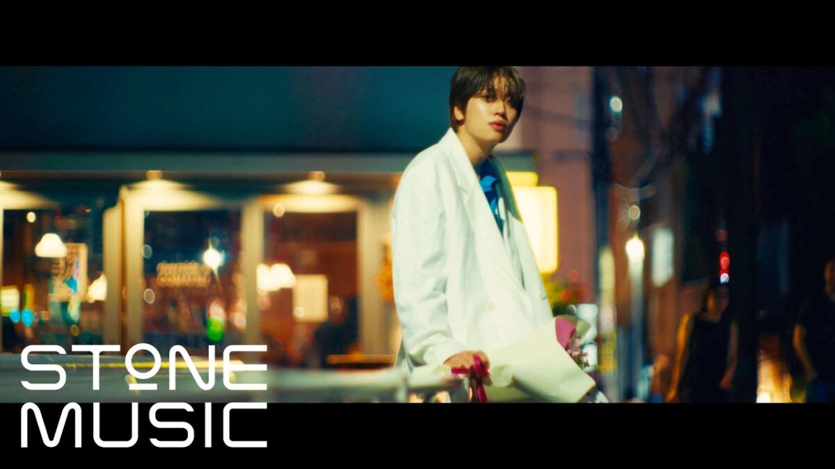 Niel, do Teen Top, em traje branco, segurando flores em uma rua iluminada à noite.