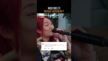 Cantor com cabelo vermelho segurando um microfone, sorrindo enquanto se apresenta em um ambiente descontraído.