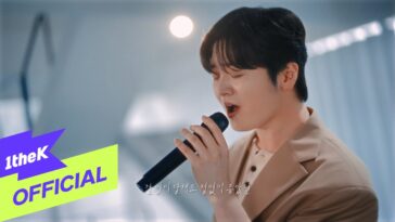 Hwang Karam canta ao vivo, segurando um microfone e expressando emoção em um cenário iluminado.