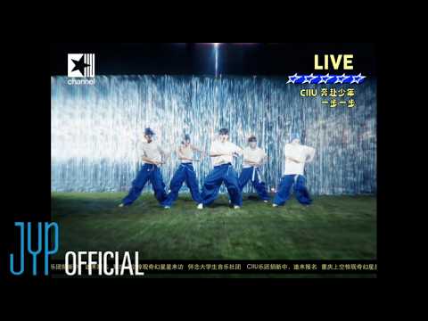 Grupo de dançarinos em coreografia animada, com luzes e um fundo brilhante em um clipe musical.