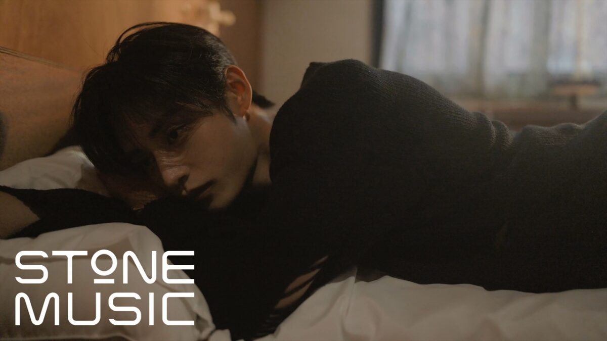 Kim Ji Woong reclina em uma cama, com expressão pensativa, em um ambiente com luz suave e aconchegante.