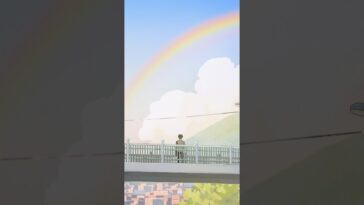 Um jovem observa um arco-íris enquanto está em uma ponte, com montanhas e nuvens ao fundo.