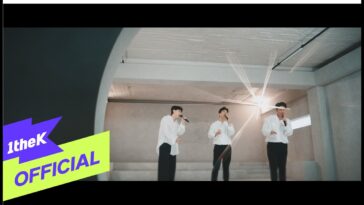 Três cantores em camisas brancas se apresentam em um espaço minimalista, com microfones e iluminação suave.