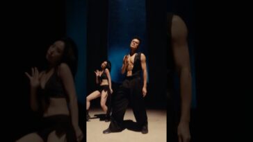 J.Y. Park e uma dançarina se apresentam em uma coreografia vibrante, com iluminação dramática e figurinos ousados.