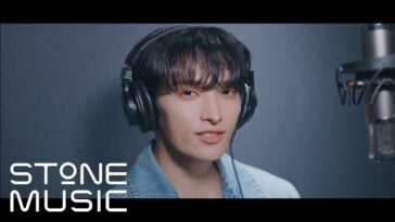 Dokyeom sorrindo enquanto usa fones de ouvido em estúdio de gravação, com microfone ao fundo.